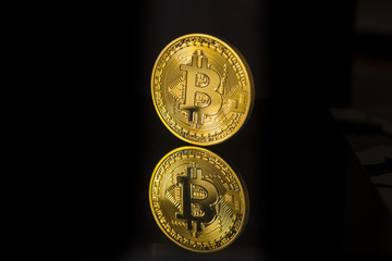 Single bitcoin coin or icon standing in sharp focus on a reflective surface with black background