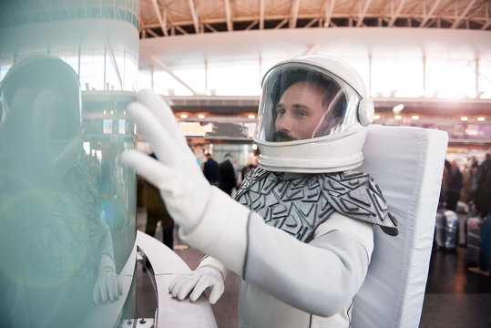 Curious man wearing white armor and helmet is standing near glass wall and looking with great interest. Waist up portrait. Copy space on left side