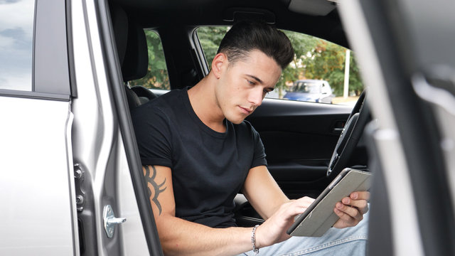 Handsome young man in casual clothes sitting in his car and using tablet PC.