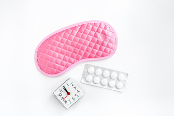 Sleeping pills for insomnia near sleep mask and alarm clock on white background top view