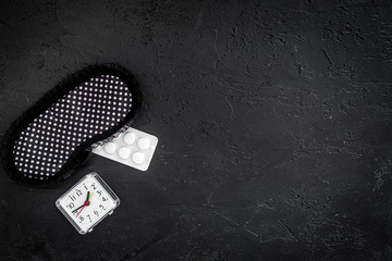 Combat insomnia. Sleeping pills near sleep mask and alarm clock on black background top view...