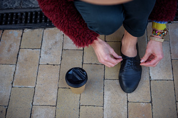 Top view close up of female leg and hands tying laces on black shoe. Woman is kneeling on alley...
