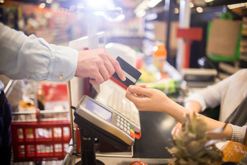 Side view close up of unrecognizable customer handing credit card to cashier paying via bank...