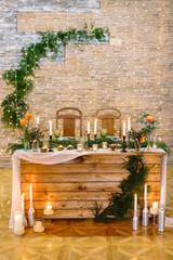 celebrating, restaurant, design concept. wedding table for two newlyweds decorated with lots of candles in holders and in silver bottles, flowers and branches of conifers