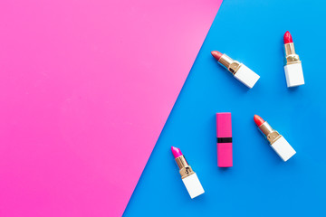 Decorative cosmetics concept. Lipsticks assorted colors and nail polish on pink and blue background top view copyspace