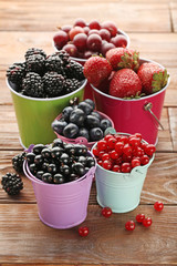 Ripe and sweet berries in buckets on wooden table