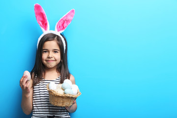 Beautiful little girl with rabbit ears and easter eggs on blue background
