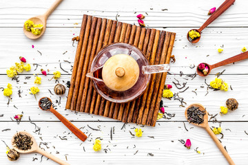 Brew the aromatic tea. Tea pot near wooden spoons with dried tea leaves, flowers and spices on white wooden background top view