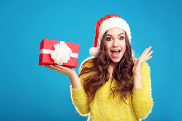 Obraz premium Beautiful young girl holding gift box on blue background