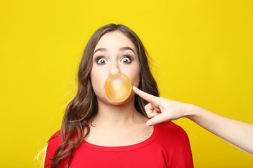 Beautiful young girl blowing bubble with chewing gum on yellow background