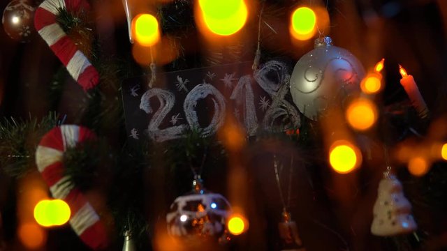 Plate numbered 2018 on a Christmas tree among toys and yellow electric lights, New Year's background.