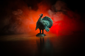 Statue of Turkey Tom strutting his stuff with red wattles and blue/white head on a smoke toned dark background. With empty space for thanks giving day greeting card