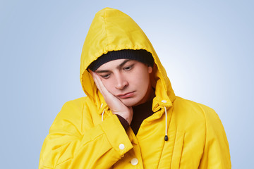 Isolated shot of pensive thoughtful man looks unhappily down, has toothache, keeps hand on cheek,...