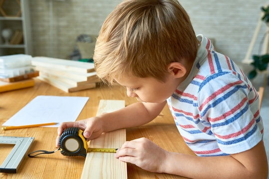 Side view portrait of cute little boy working with wood sitting at table and taking measurements  making wooden model