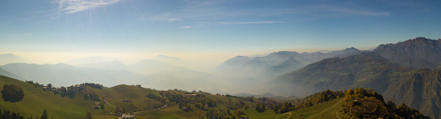 Fototapeta premium Landscape on hills and Orobie mountains with humidity in the air and pollution. Panorama from Farno Mountain, Bergamo, Italy