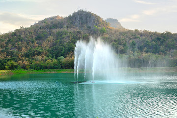 The fountain in the  public park has a mountain  background.