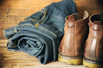 Blue jeans and brown leather men's boots on a wooden surface, close up