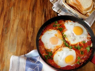 Aluminium Prints Fried eggs A pan of fried eggs with tomato sauce and parsley on a wooden background. Shakshuka a traditional meal of the Jewish cuisine