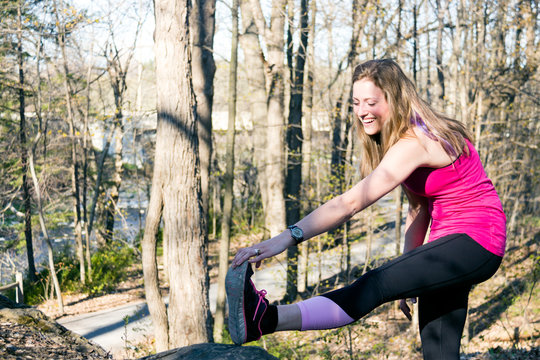 Fit girl stretches leg before running in the woods