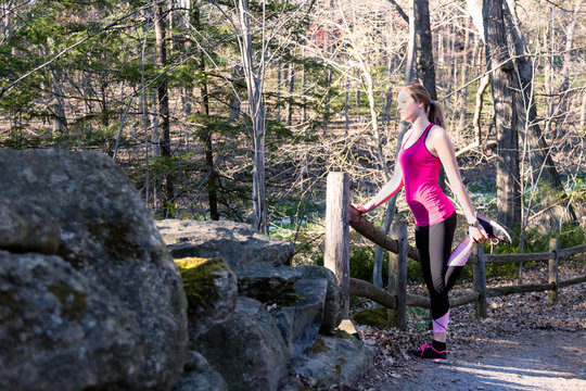 Fitness woman in the forest stretching legs before jogging