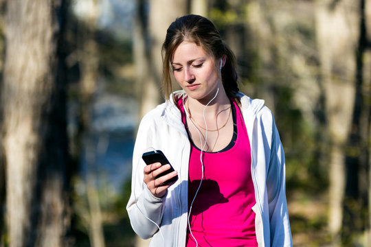 Young woman selects music on smartphone prior to running in nature