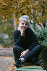 portrait of a young women sitting and smiling on a bench in park on autumn day 