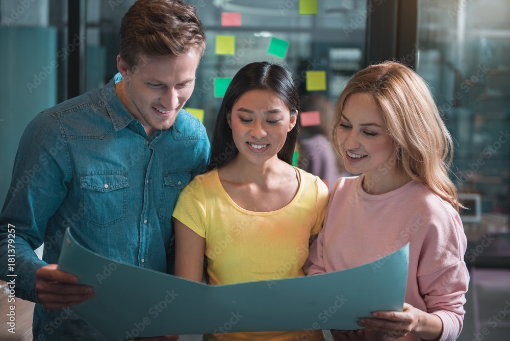 Poster new start-up. joyful man and women are standing in office and holding paper sheet while looking at i