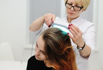 Fototapeta premium Doctor examines scalp a pretty young girl with special instrument UV lamp. Skin problems, dermatology, shingles, psoriasis, redness, prevention