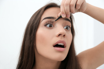 Fototapeta premium Young woman removing artificial eyelashes on light background