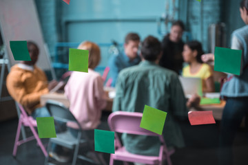 Group of colleagues working with each other while sitting at desk in wide room. Bright stickers...