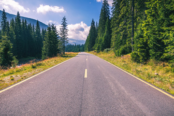 Mountain road. Landscape with rocks, sunny sky with clouds and beautiful asphalt road in the evening in summer. Vintage toning. Travel background. Highway in mountains. Transportation