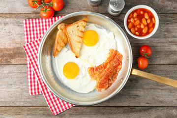 Frying pan with eggs, toasts and bacon on table