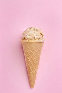 Waffle cone with caramel ice cream on color background
