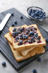 Board with tasty toasts, jam and blueberries on table