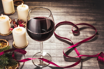 Glass of wine and burning candles. Red wine on wooden grey background. Slices  of dried orange. Heart ribbon bow