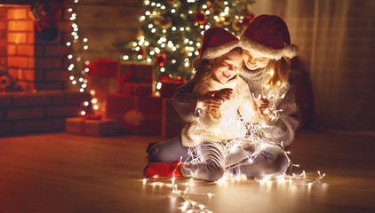 Merry Christmas! mother and child daughter with glowing garland near tree