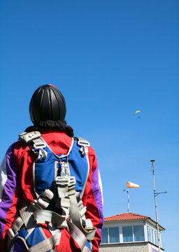 unrecognizable skydiver in unifor stands and looks at the paratroopers. Control tower and wind direction indicator in the foreground