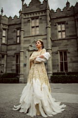 Fototapeta premium Beautiful sexy woman is wearing princess dress with feathers staying infront of castle