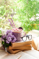 Coffee cup with marshmallow, open book and flowers bouquet on window sill. Feminine background. Breakfast, reading, spring and education concept