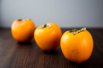 Three ripe persimmons on a dark wooden background