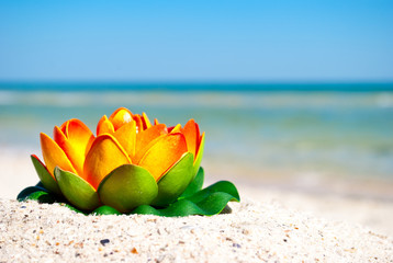large orange lotus flower with green leaves lies on yellow sand on a background of blue sea and a white wave blue sky summer vacation vacation summer day heat beach beach