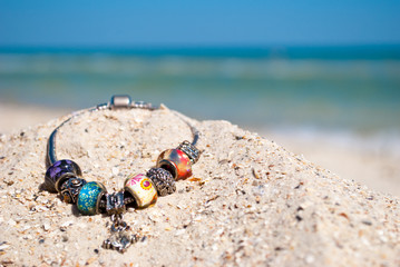 beautiful female bracelet decoration jewelry with large beads and rhinestones lies on the yellow sand summer beach sea shore blue sky vacation vacation weekend