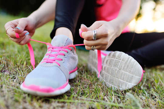 Girl ties up shoelaces on sneakers before running or before fitness training on the background of nature