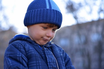 Portrait of adorable little kid boy with long blond hair playing with snowballs outdoors..Child with blue scarf and hat walking and having fun on a windy winter day.