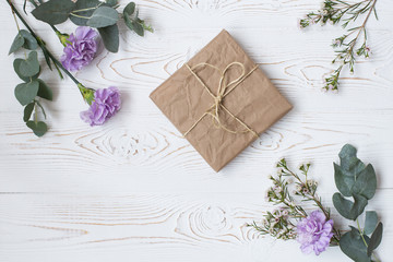 Gift or present box wrapped in kraft paper and flower on white table from above. Flat lay styling. Copy space for text.