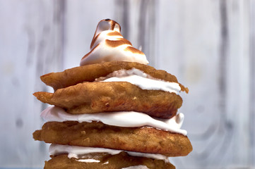A stack of appetizing fried fritters with cream. Cream of egg white. Baked French / Italian meringue with crispy crust. Pancakes are greased with whipped cream. Mini cake with cream.