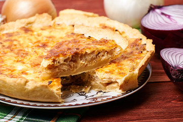 Appetizing French onion pie in a cut. Portion of vegetable vegetarian pie with cheese crust. The table is served for dinner. Simple rustic homemade food.