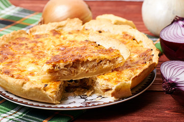 Appetizing French onion pie in a cut. Portion of vegetable vegetarian pie with cheese crust. The table is served for dinner. Simple rustic homemade food.