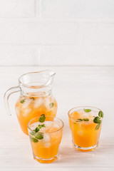 Mandarin cocktail with ice and mint in beautiful glasses and jug, fresh ripe citrus on white wooden background. Sweet orange juice. Close up photography. Selective focus