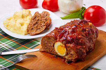 Traditional Cuban meatloaf pulpeta with an egg in the middle. Delicious, hearty lunch. Mashed potatoes with a large meat roll. Fresh vegetables in the background.